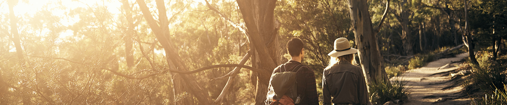 two people walking together down a trail at sunset