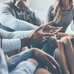 A group of people sitting together with one person expressive through their hands